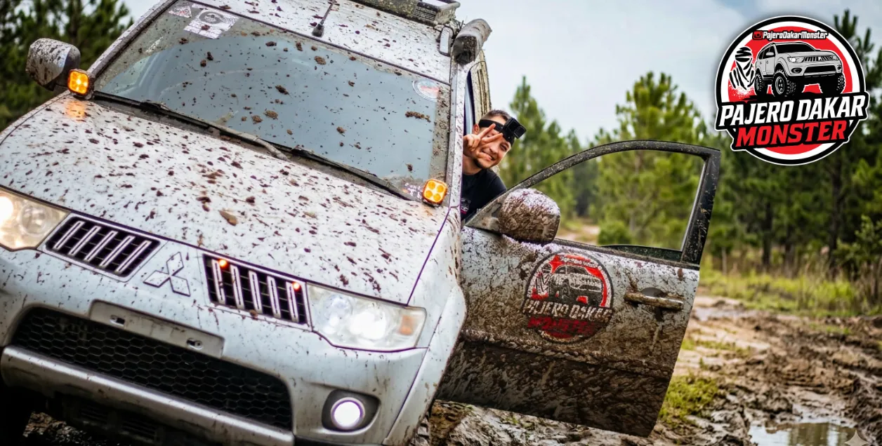 Pajero coberta de lama e piloto sorrindo pela janela, com o logo Pajero Dakar Monster